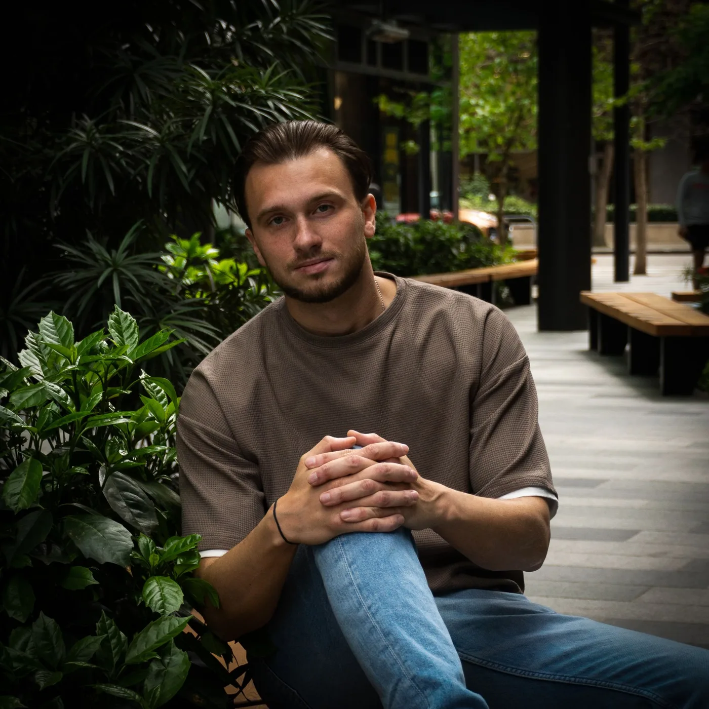 Danil Maslov seated outdoors among green foliage in a city courtyard